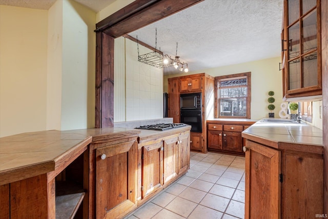 kitchen with tile counters, brown cabinets, a sink, and a textured ceiling