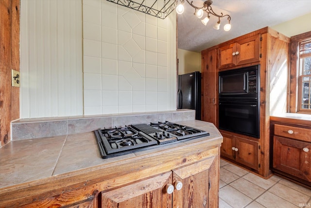 kitchen featuring tasteful backsplash, brown cabinetry, light countertops, black appliances, and light tile patterned flooring