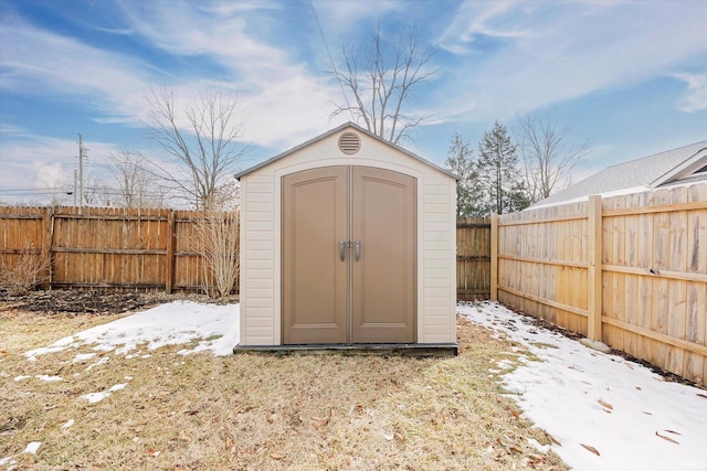 snow covered structure with an outbuilding, a fenced backyard, and a storage unit