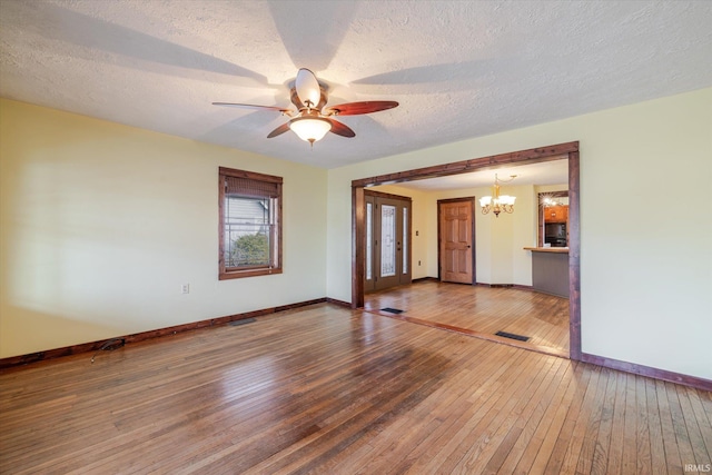 empty room featuring visible vents, hardwood / wood-style floors, a textured ceiling, baseboards, and ceiling fan with notable chandelier