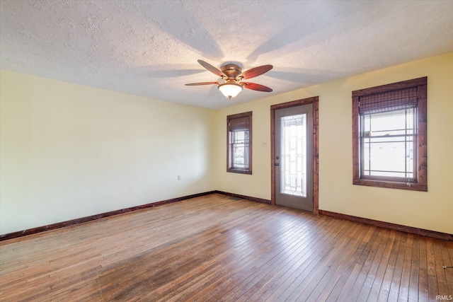 empty room with a ceiling fan, baseboards, a textured ceiling, and light wood finished floors