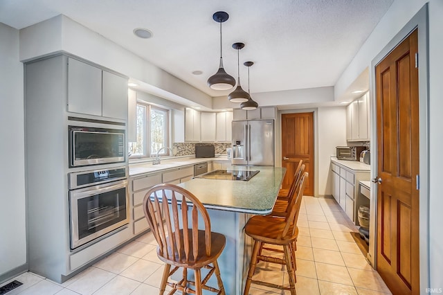 kitchen featuring tasteful backsplash, a center island, hanging light fixtures, stainless steel appliances, and light tile patterned flooring