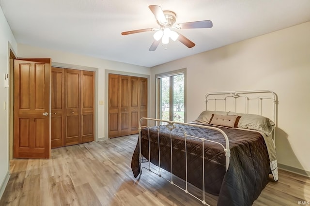 bedroom featuring light wood-style floors, baseboards, a ceiling fan, and two closets