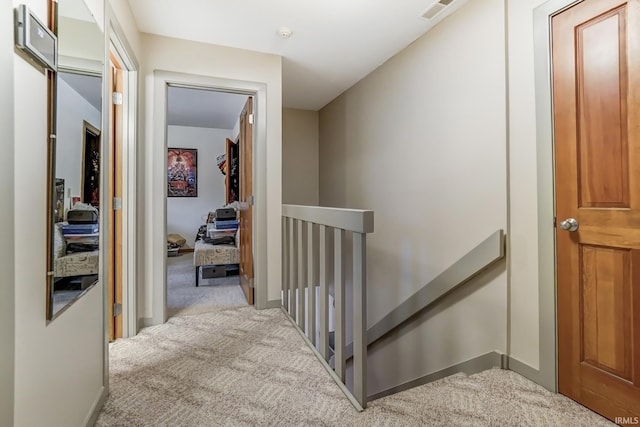 hallway with light carpet, visible vents, and an upstairs landing