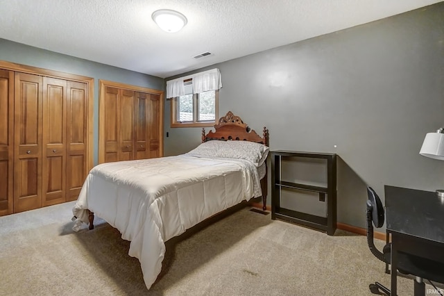 bedroom featuring light carpet, a textured ceiling, two closets, and visible vents