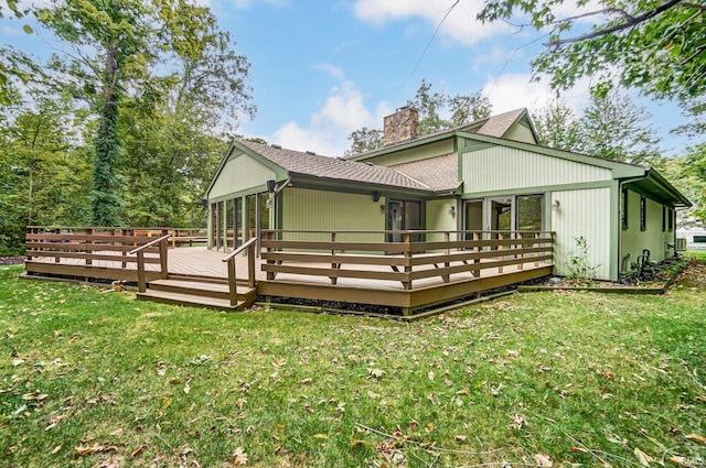 back of property with a chimney, a wooden deck, and a lawn