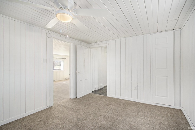 spare room featuring dark carpet, wood walls, and ceiling fan