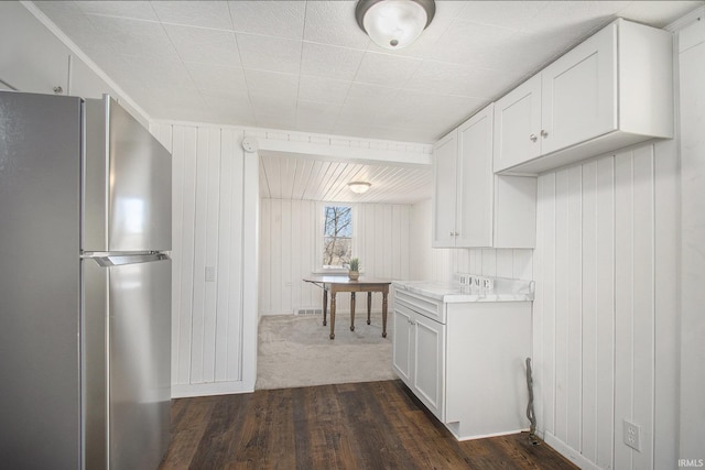 kitchen featuring dark wood-type flooring, wood walls, white cabinetry, light countertops, and freestanding refrigerator