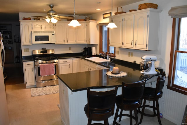 kitchen with a peninsula, white microwave, white cabinets, and gas stove