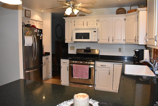 kitchen featuring dark countertops, appliances with stainless steel finishes, white cabinetry, a sink, and ceiling fan