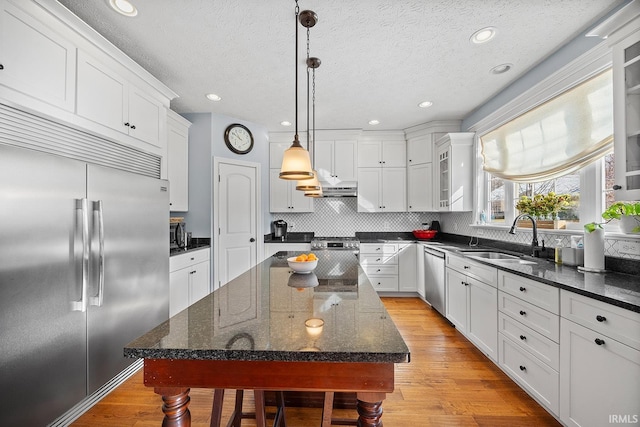 kitchen featuring a center island, stainless steel appliances, hanging light fixtures, glass insert cabinets, and a sink