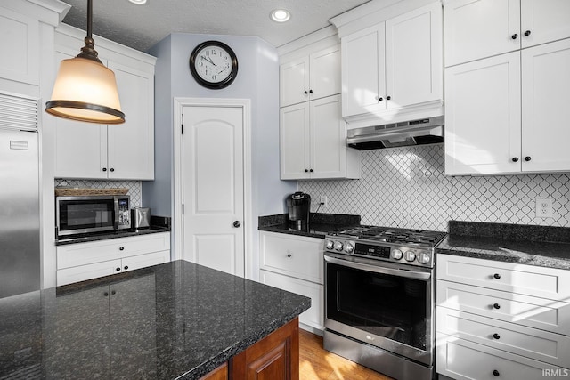 kitchen with hanging light fixtures, appliances with stainless steel finishes, white cabinets, dark stone counters, and exhaust hood