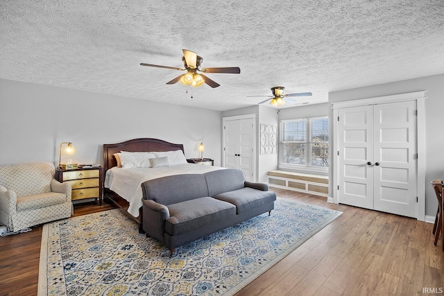 bedroom featuring multiple closets, a textured ceiling, a ceiling fan, and wood finished floors