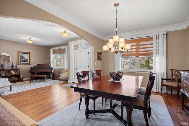 dining room featuring ornamental molding, arched walkways, an inviting chandelier, and wood finished floors