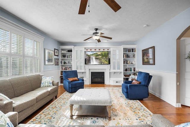 living area with arched walkways, dark wood-style flooring, a glass covered fireplace, wainscoting, and a textured ceiling