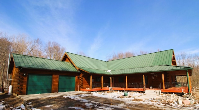 view of front of property with covered porch, log exterior, metal roof, and a garage