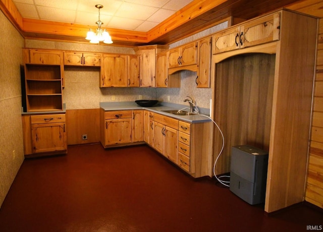 kitchen featuring a raised ceiling, hanging light fixtures, light countertops, a chandelier, and a sink