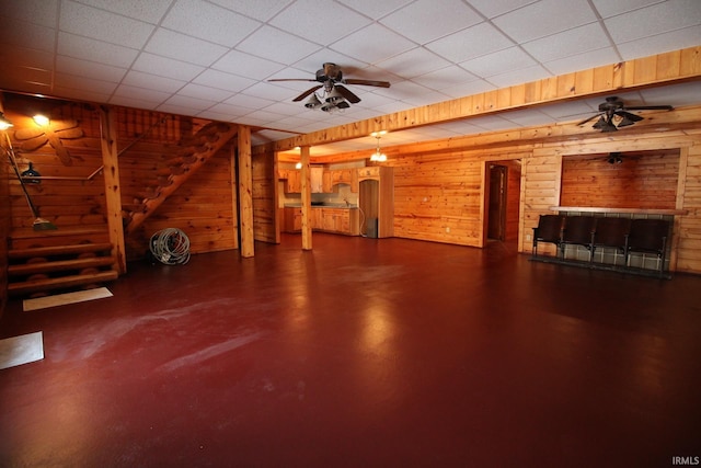 finished below grade area featuring wood walls, ceiling fan, stairs, and a drop ceiling