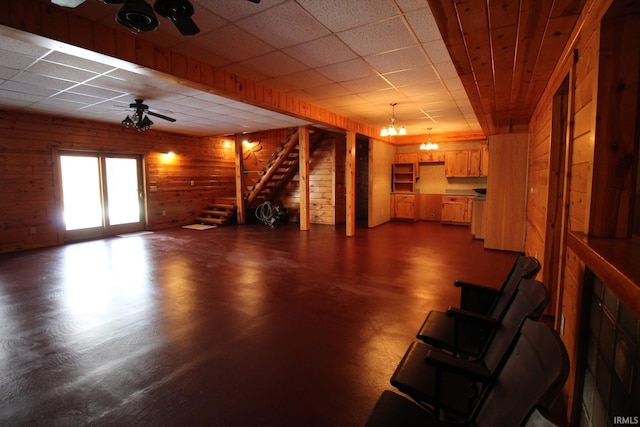 unfurnished living room featuring concrete flooring, ceiling fan, wood walls, and stairs