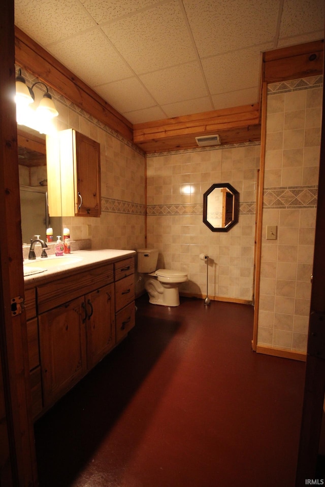 bathroom with toilet, tile walls, a paneled ceiling, and vanity