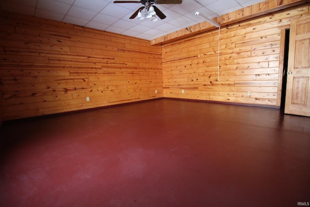 empty room with wooden walls, ceiling fan, and finished concrete floors