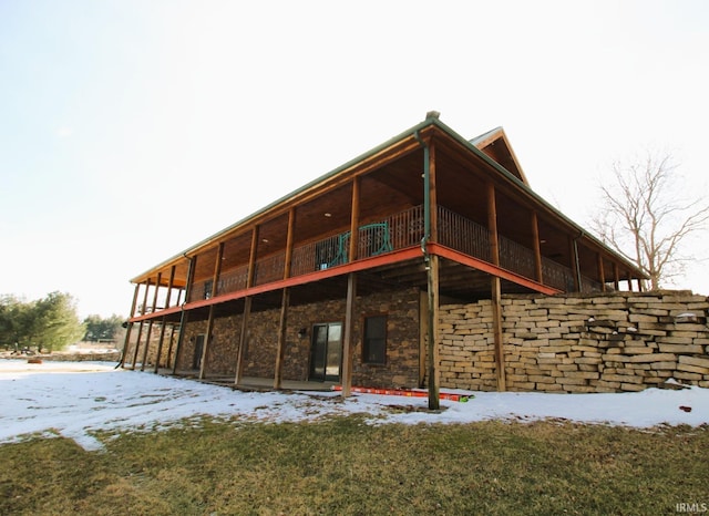 snow covered back of property with stone siding