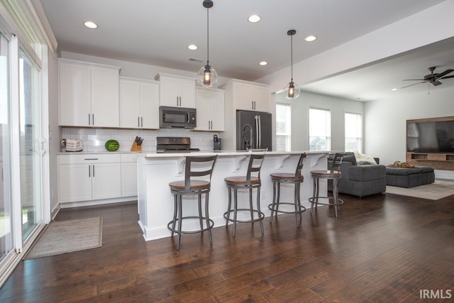 kitchen with a center island with sink, stainless steel refrigerator, hanging light fixtures, light countertops, and black microwave