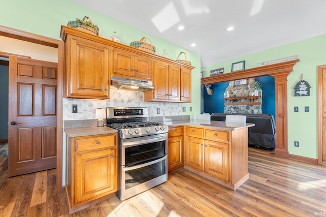 kitchen featuring under cabinet range hood, a peninsula, open floor plan, light wood-type flooring, and double oven range