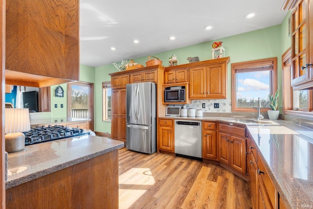 kitchen with appliances with stainless steel finishes, brown cabinetry, light wood finished floors, and light stone counters