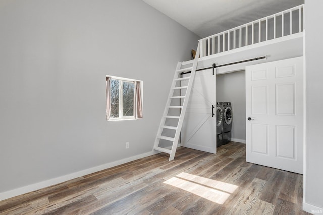 unfurnished bedroom with a towering ceiling, a barn door, wood finished floors, washer and dryer, and baseboards