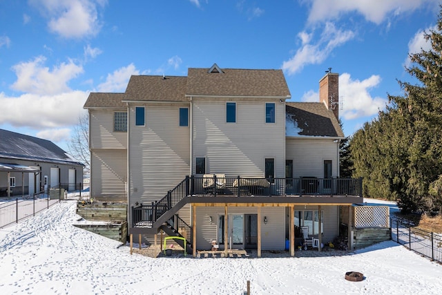 snow covered house featuring a deck, stairway, a chimney, and fence