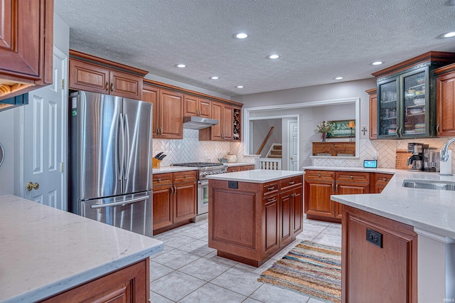 kitchen with glass insert cabinets, appliances with stainless steel finishes, a center island, under cabinet range hood, and a sink