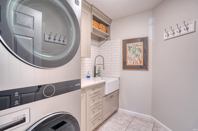 washroom featuring cabinet space, a textured ceiling, stacked washing maching and dryer, a sink, and light tile patterned flooring