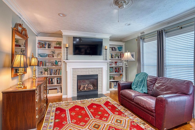 living area with ornamental molding, a textured ceiling, a tiled fireplace, and wood finished floors