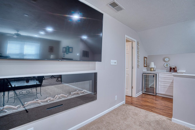 bar featuring beverage cooler, visible vents, a bar, lofted ceiling, and carpet floors