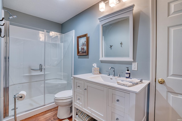 full bath with a textured ceiling, toilet, wood finished floors, vanity, and a shower stall