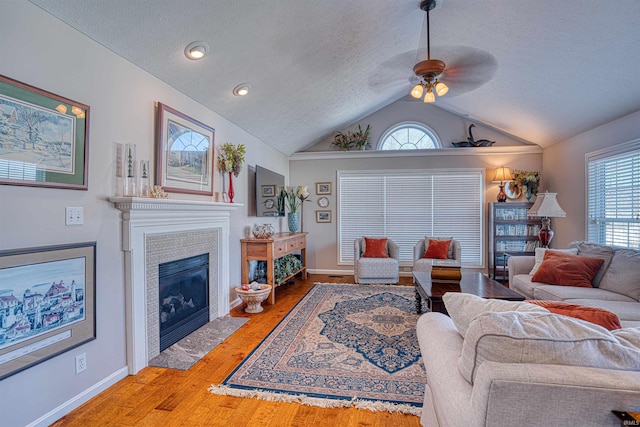 living area with lofted ceiling, a textured ceiling, wood finished floors, a fireplace with flush hearth, and baseboards