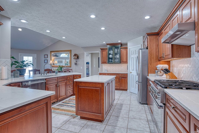 kitchen featuring glass insert cabinets, appliances with stainless steel finishes, a center island, under cabinet range hood, and a sink