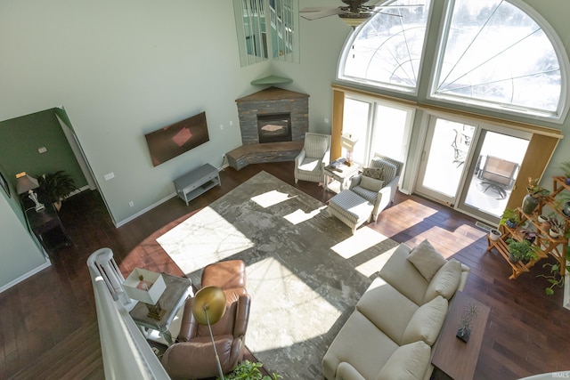 living area with ceiling fan, a high ceiling, a fireplace, baseboards, and dark wood finished floors