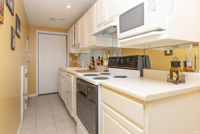 kitchen featuring light tile patterned flooring, under cabinet range hood, white appliances, a sink, and light countertops