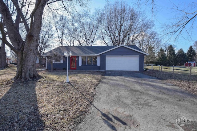 single story home with aphalt driveway, an attached garage, and fence