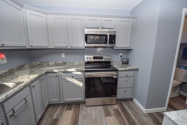 kitchen featuring baseboards, dark wood-style floors, appliances with stainless steel finishes, gray cabinetry, and a sink