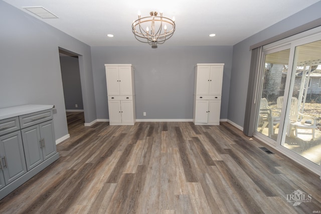 unfurnished dining area with an inviting chandelier, baseboards, visible vents, and dark wood-style flooring