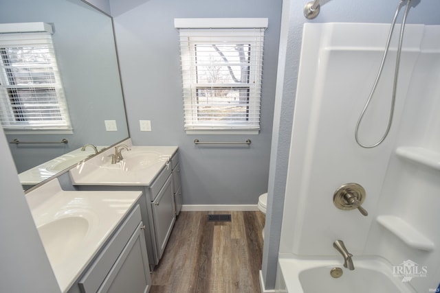 bathroom featuring baseboards, toilet, vanity, wood finished floors, and shower / bathtub combination