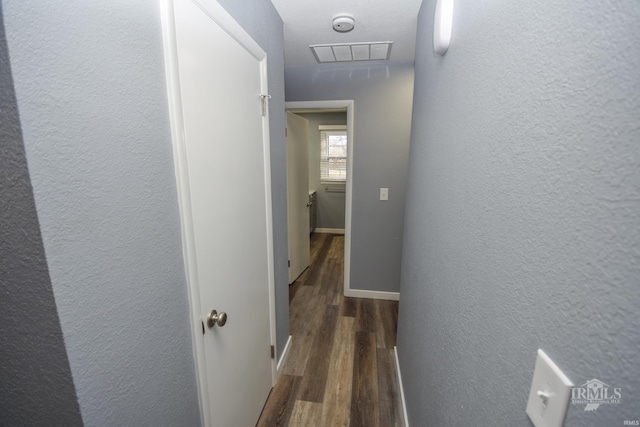 hallway with a textured wall, dark wood finished floors, visible vents, and baseboards