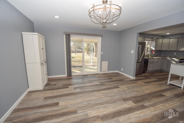 unfurnished dining area with baseboards, recessed lighting, dark wood finished floors, and an inviting chandelier