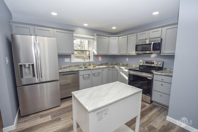 kitchen featuring appliances with stainless steel finishes, wood finished floors, a center island, gray cabinets, and a sink