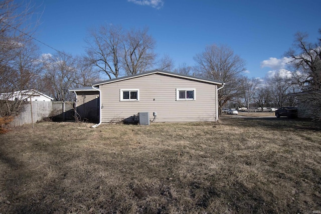 back of property with central AC unit, fence, and a yard