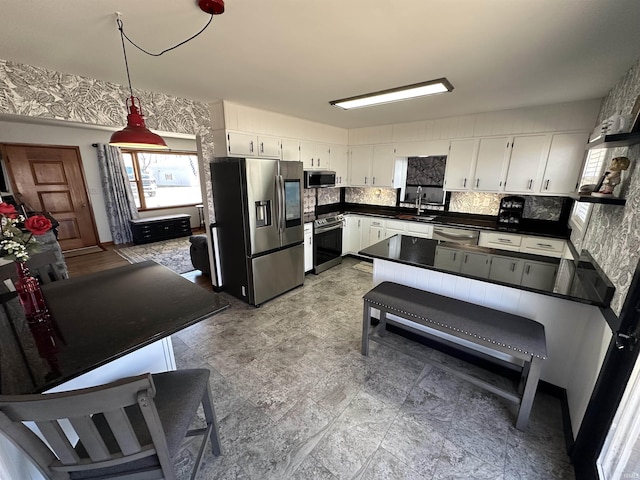 kitchen with dark countertops, backsplash, appliances with stainless steel finishes, white cabinetry, and a sink