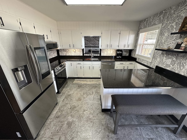 kitchen featuring dark countertops, stainless steel appliances, white cabinetry, open shelves, and a sink